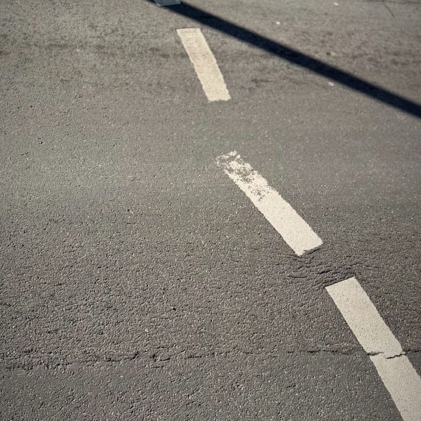 Straße mit abgenutzten, weißen Fahrbahnmarkierungen auf grauem Asphalt.