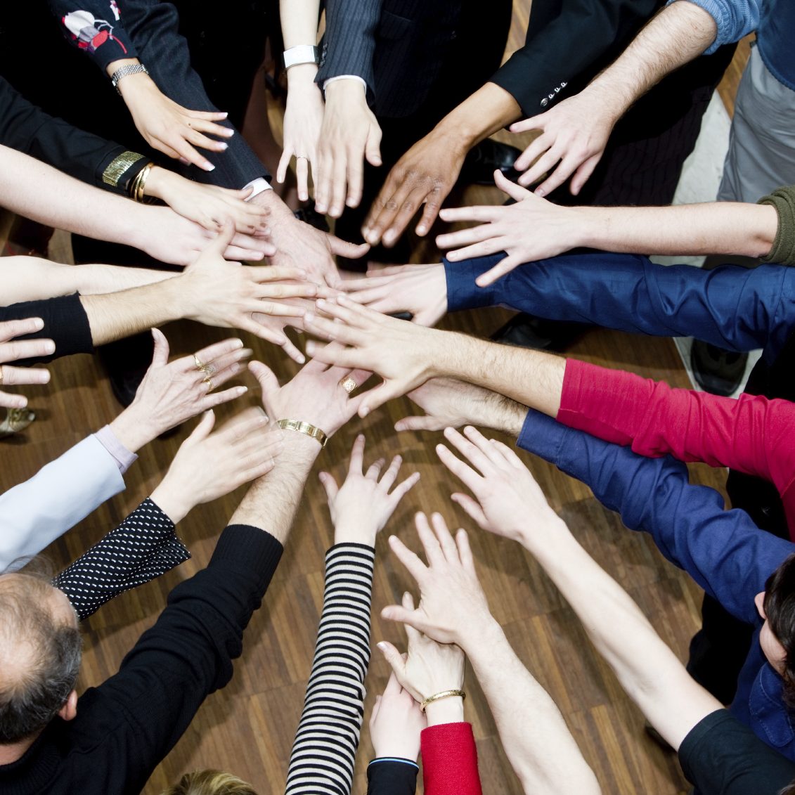Viele Hände verschiedener Personen, die sich gemeinsam in der Mitte treffen.
